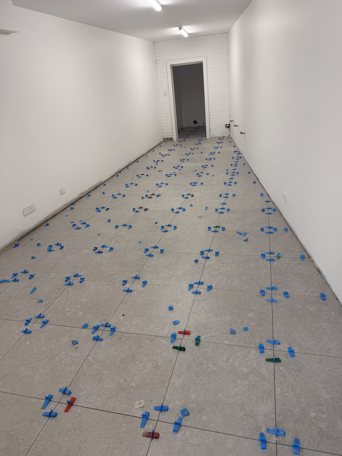Large-format floor tiles set out with spacers in an empty commercial corridor