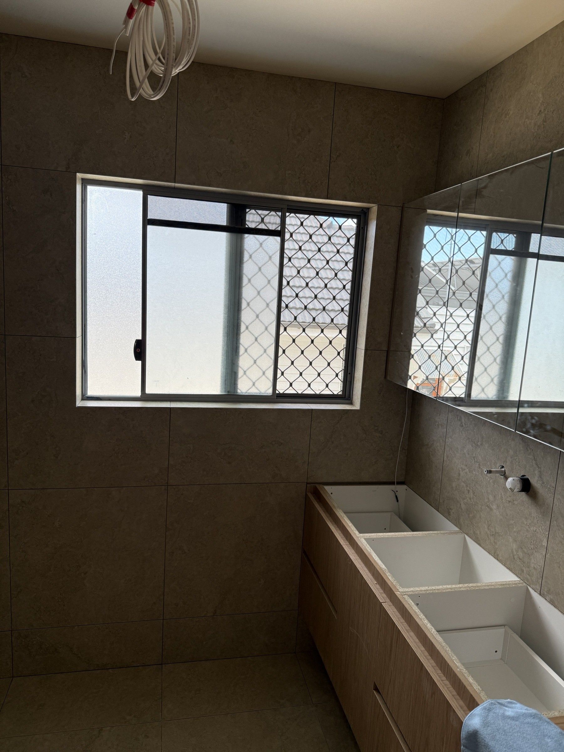 Tiled bathroom wall nearing completion, with window and vanity cabinetry