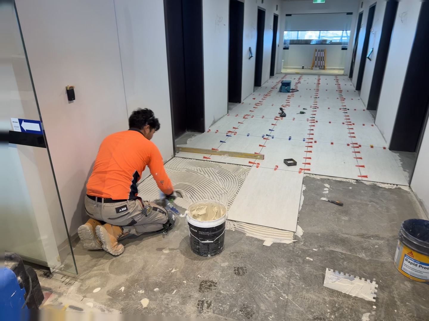 Tiler setting out large-format floor tiles in a commercial corridor