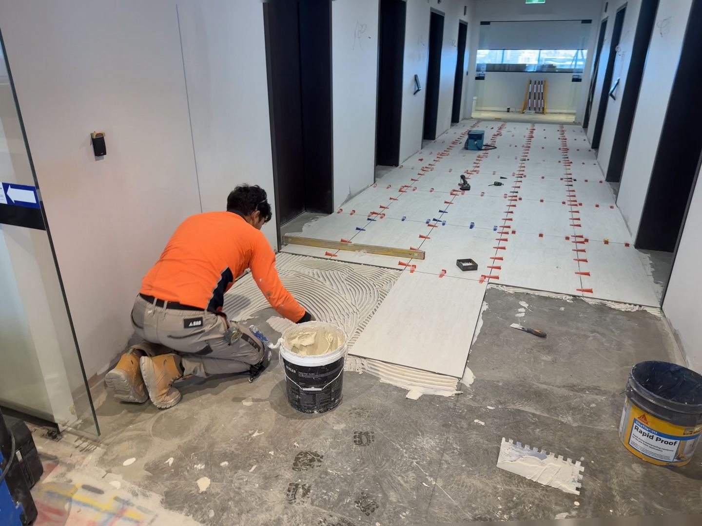 Tiler laying large-format floor tiles in a commercial corridor