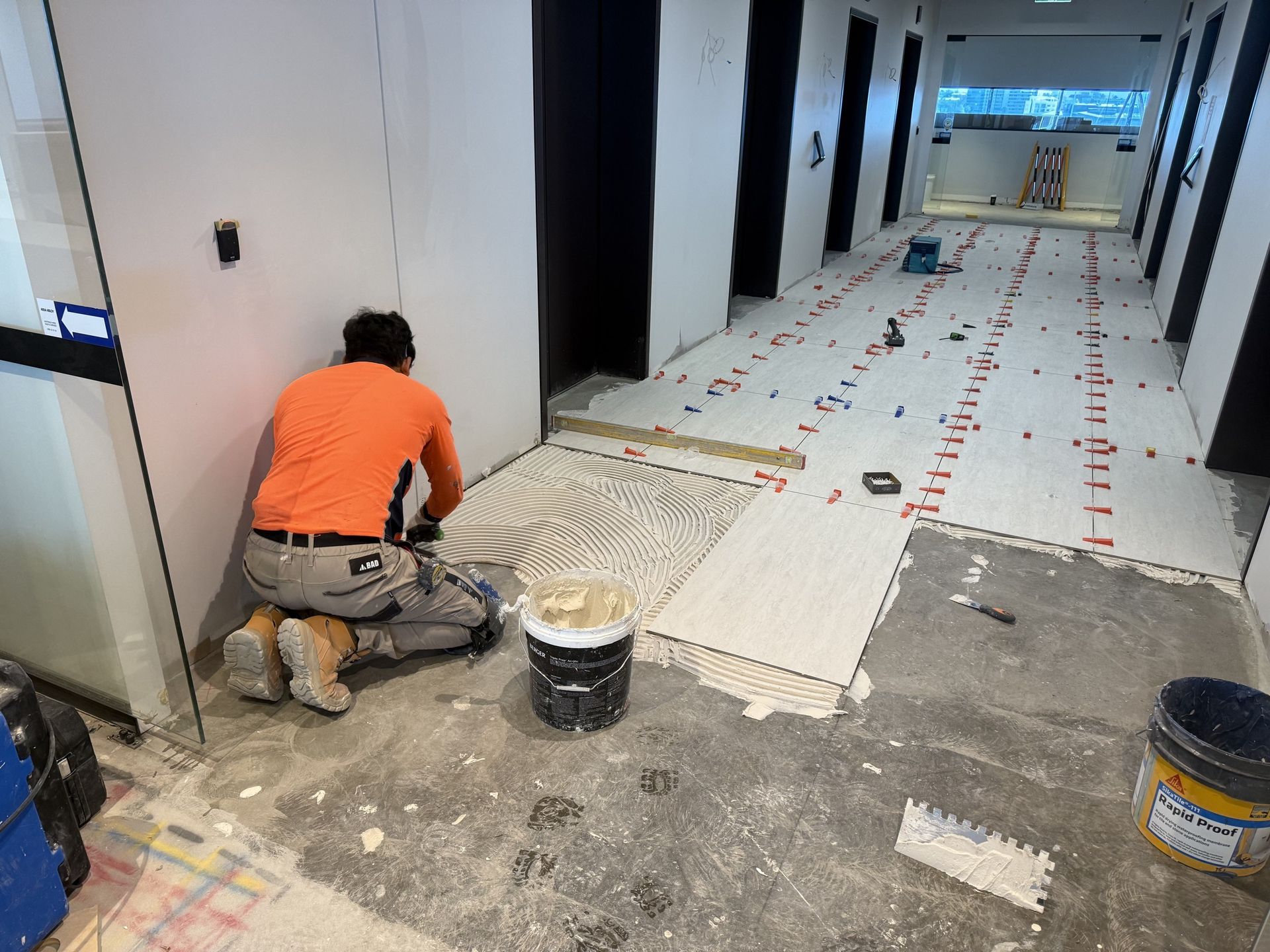 Large-format floor tiles being set out with levelling clips in a commercial lift lobby