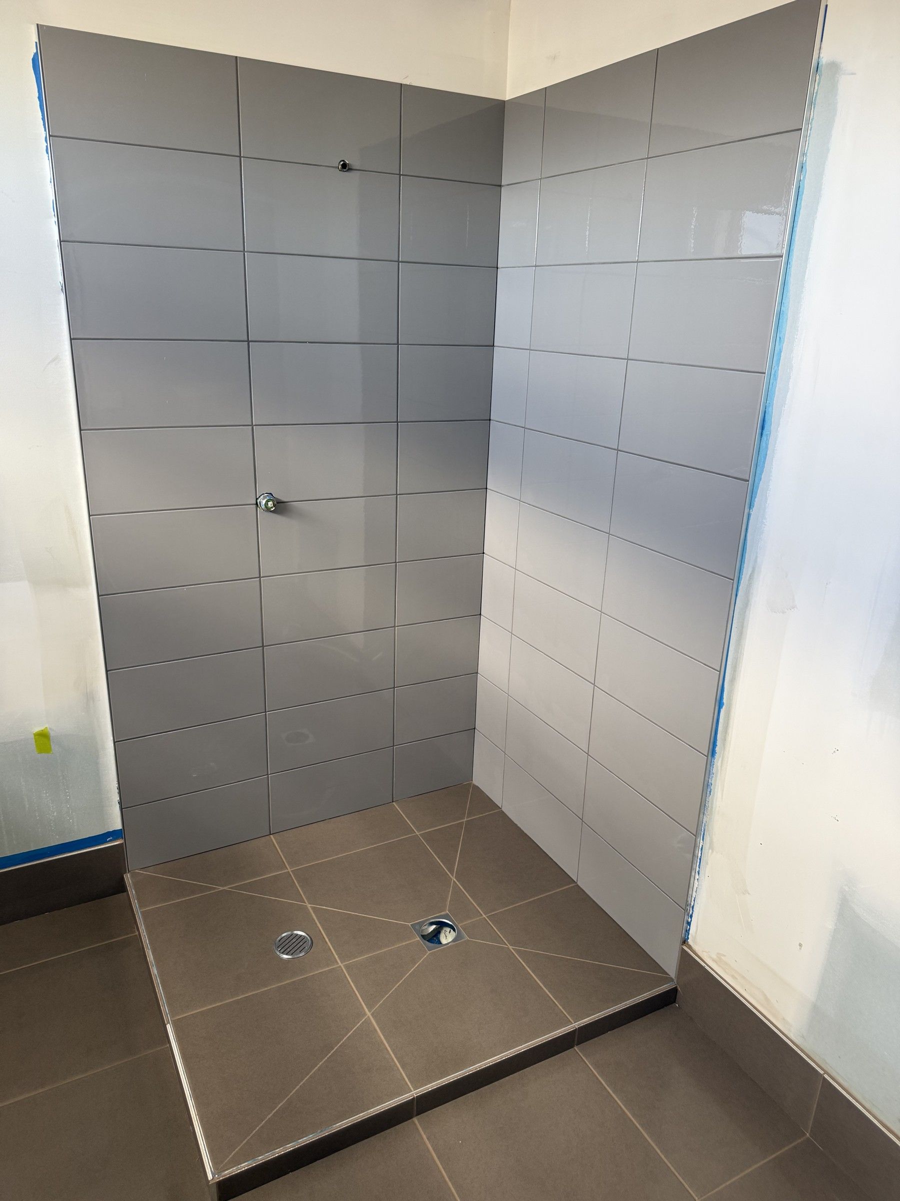 Glossy grey wall tiling in a shower recess, with brown floor tiling